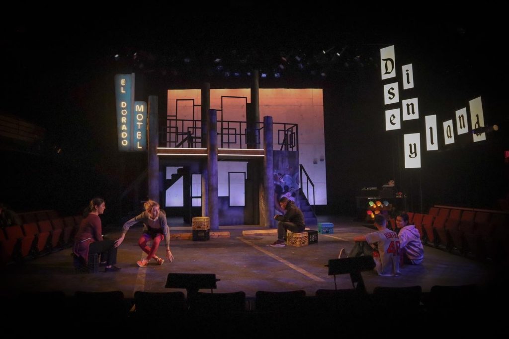 The set of the play "somebody's children" on a dark stage. A bare motel, with a large Bright Disneyland sign on the side.