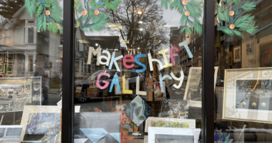 Image of Makeshift Gallery's front window, with the hand-made paper Makeshift Gallery sign in multiple colors hung above the arts display.