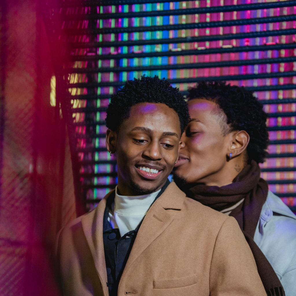 Positive Black Same-Sex Couple Embracing Gently Against Colorful Wall