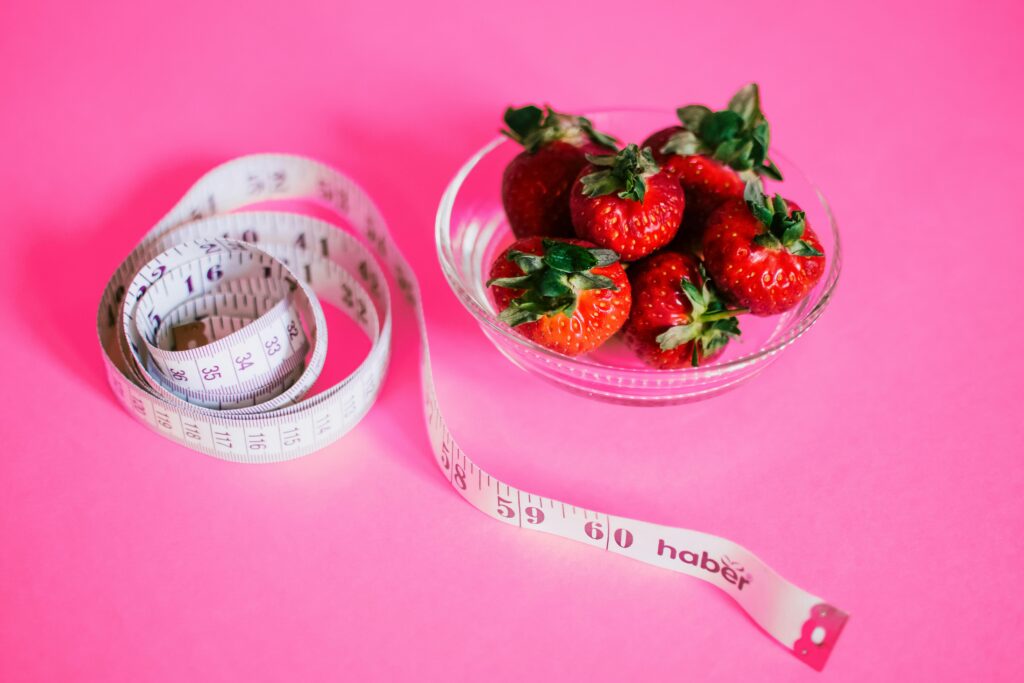 A measuring tape next to a bowl of strawberries
