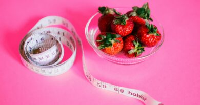 A measuring tape next to a bowl of strawberries